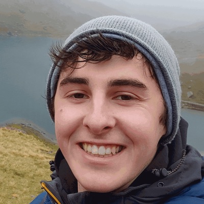 Tyr, smiling in a woolly hat on a misty hillside above a lake